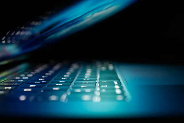 A backlit laptop keyboard glowing blue in a dark room, illustrating bulk distribution list migration to Exchange Online with PowerShell.